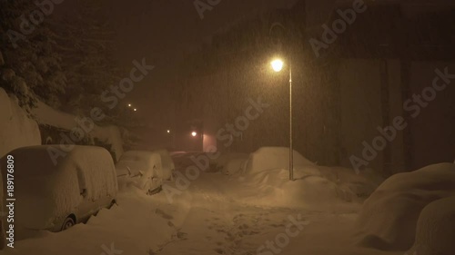 Cars under street lamps covered in deep snow winter blizzard