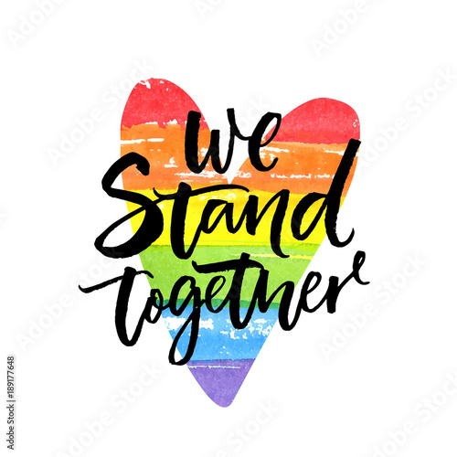 We stand together. Inspirational LGBT slogan han dwritten on rainbow flag heart.