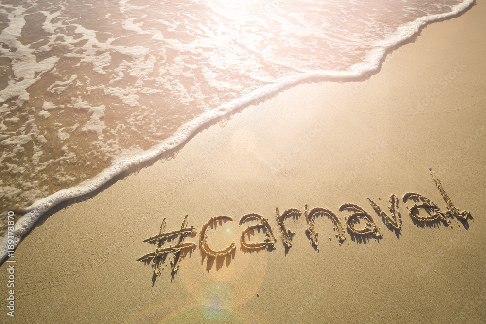 Fototapeta premium Modern message for Carnaval with a social media-friendly hashtag written on smooth sand beach