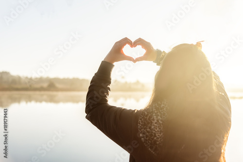 Woman's hands forming a heart shape on morning sunrise.