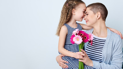 Happy Mother's Day, Women's day or Birthday background. Cute little girl giving mom bouquet of pink gerbera daisies. Loving mother and daughter smiling and hugging.