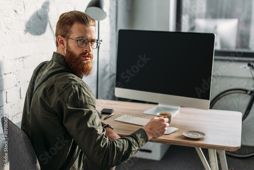 serious bearded businessman holding cup of coffee and looking at camera © LIGHTFIELD STUDIOS