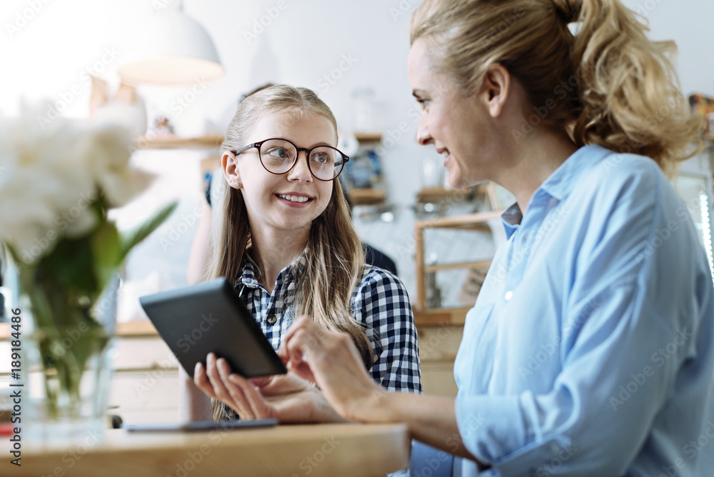 Fototapeta premium Just listen. Delighted female person talking to her daughter and holding tablet while sitting in semi position