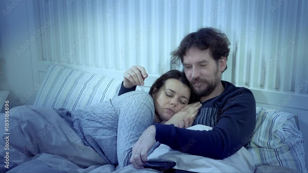 Man checking message on phone while woman is sleeping betrayal Man checking message on phone while woman is sleeping betrayal