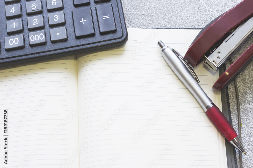 Business Workplace, Analysis, Finance Concept with a calculator, an opened planner and a paper stapler, close up, grey concrete background Business Workplace, Analysis, Finance Concept with a calculator, an opened planner and a paper stapler, close up, grey concrete background