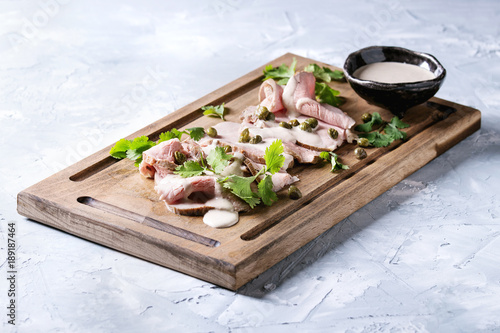 Vitello tonnato italian dish. Thin sliced veal with tuna sauce, capers and coriander served on wooden serving board over gray texture background. photo