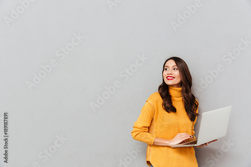 Obraz na plátně Happy brunette woman in sweater holding laptop computer