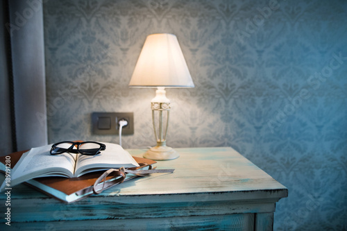 Obraz na plátně A lamp and a book on a bedside table in a hotel room.