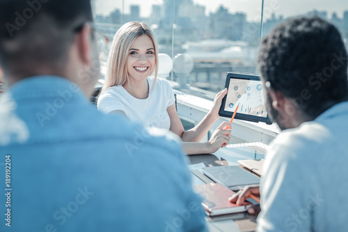 Check this out. Selective focus on an extremely happy blonde lady grinning broadly while looking at her coworkers and presenting them her project ideas.