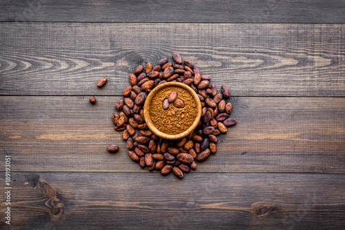 Main ingredient for chocolate. Cocoa powder in bowl near cocoa beans on dark wooden background top view copy space