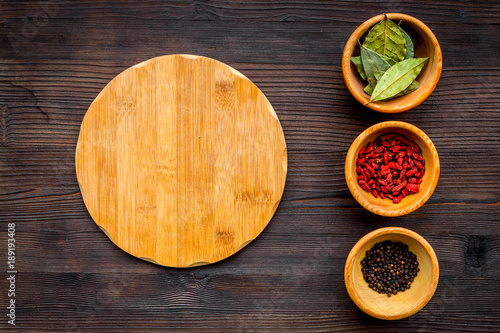 Make menu or write recipe. Mock up for menu or recipe. Wooden cutting board near ingredients in bowls bay leaf, black repper and godji on dark wooden background top view