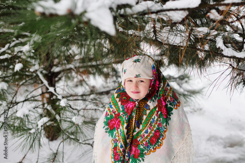 portrait of a child girl in a headscarf in the Urs style on the background of snow and forest. Russia, frost, fairy tale, carnival