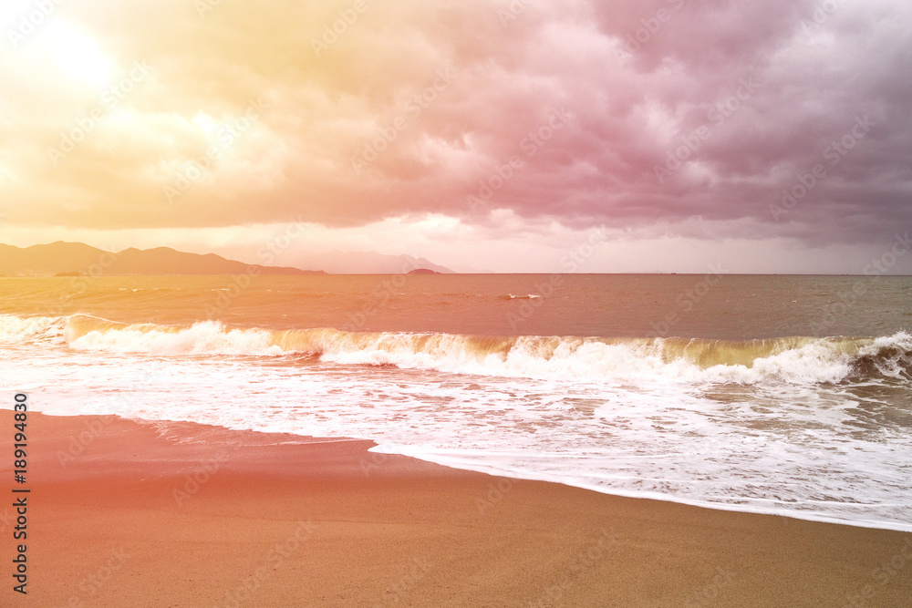 storm with big waves in the sun rays on the seashore with mountains on the background