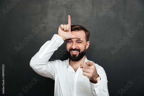 Foto Portrait of sarcastic man showing loser sign on his forehead and pointing on cam