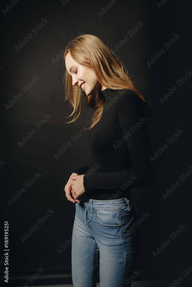 Stylish girl in a fashion. Beautiful woman in a black turtleneck stands near a background and smiles. Lady coquettishly tilted her head down and rejoices. Stylish girl in a fashion. Beautiful woman in a black turtleneck stands near a background and smiles. Lady coquettishly tilted her head down and rejoices.