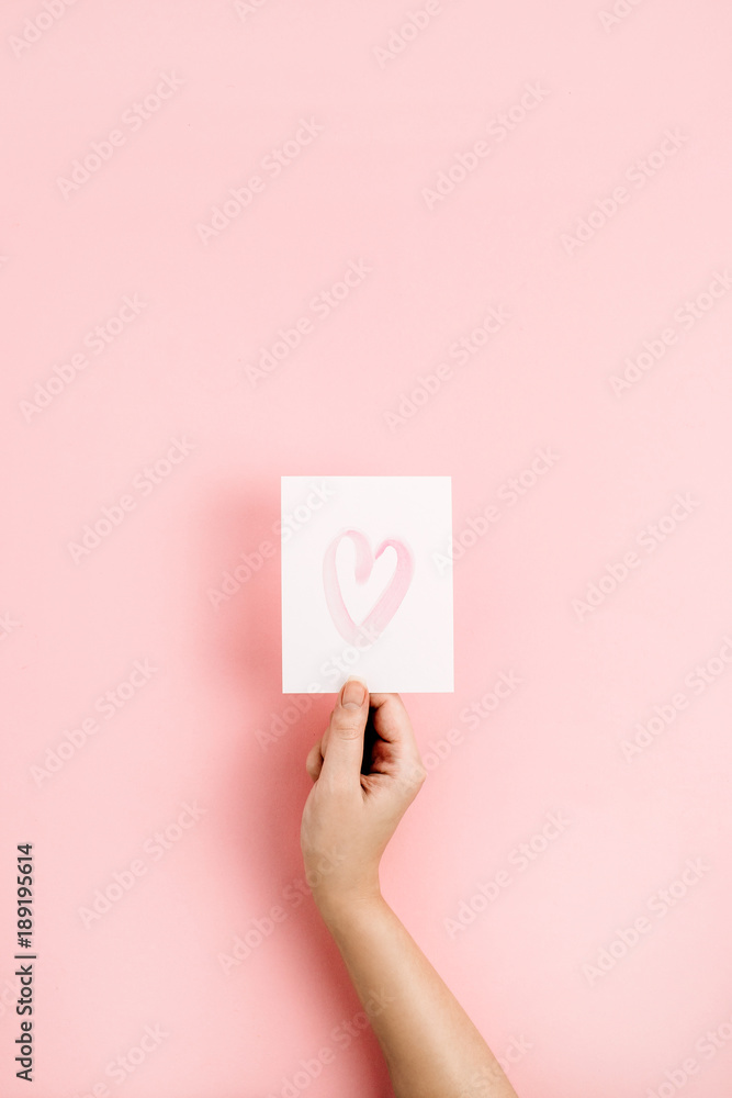 Valentine's Day composition. Female hand holding card with heart symbol on pale pink background. Flat lay, top view Love concept. Valentine's Day composition. Female hand holding card with heart symbol on pale pink background. Flat lay, top view Love concept.