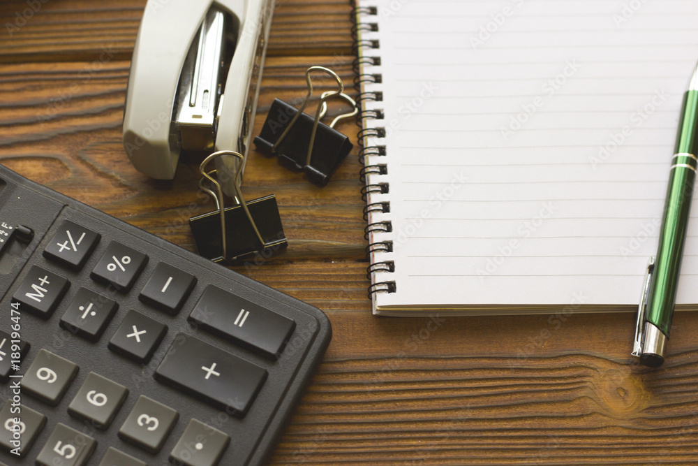 Business Office Workplace Concept with an opened planner, stapler, paper clips and calculator on a wooden table, close up Business Office Workplace Concept with an opened planner, stapler, paper clips and calculator on a wooden table, close up