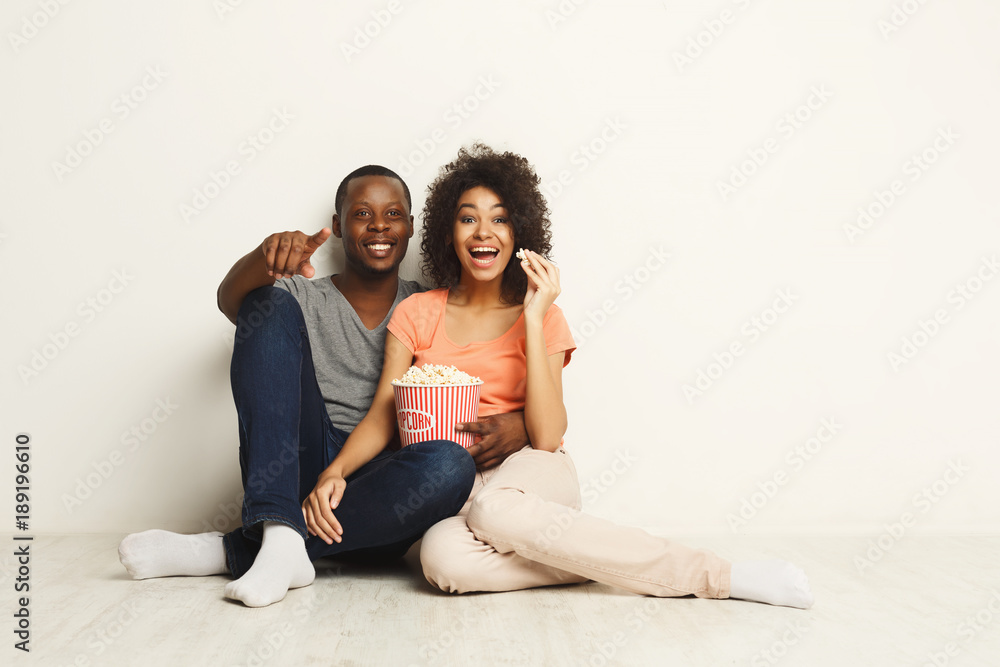 Smiling black couple wathing movie at home on the floor Smiling black couple wathing movie at home on the floor