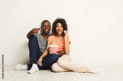 Smiling black couple wathing movie at home on the floor © Prostock-studio