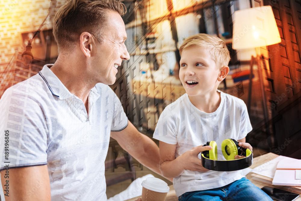 Excited child. Surprised emotional boy looking at his father while holding new amazing headphones and feeling excited about it Excited child. Surprised emotional boy looking at his father while holding new amazing headphones and feeling excited about it