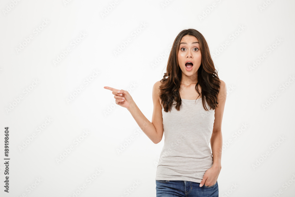 Shocked brunette woman with arm in pocket pointing on copyspace Shocked brunette woman with arm in pocket pointing on copyspace