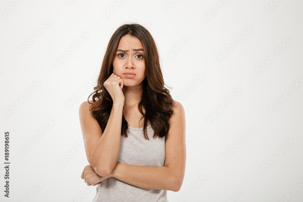 Confused brunette woman with arm near chin looking at camera Confused brunette woman with arm near chin looking at camera