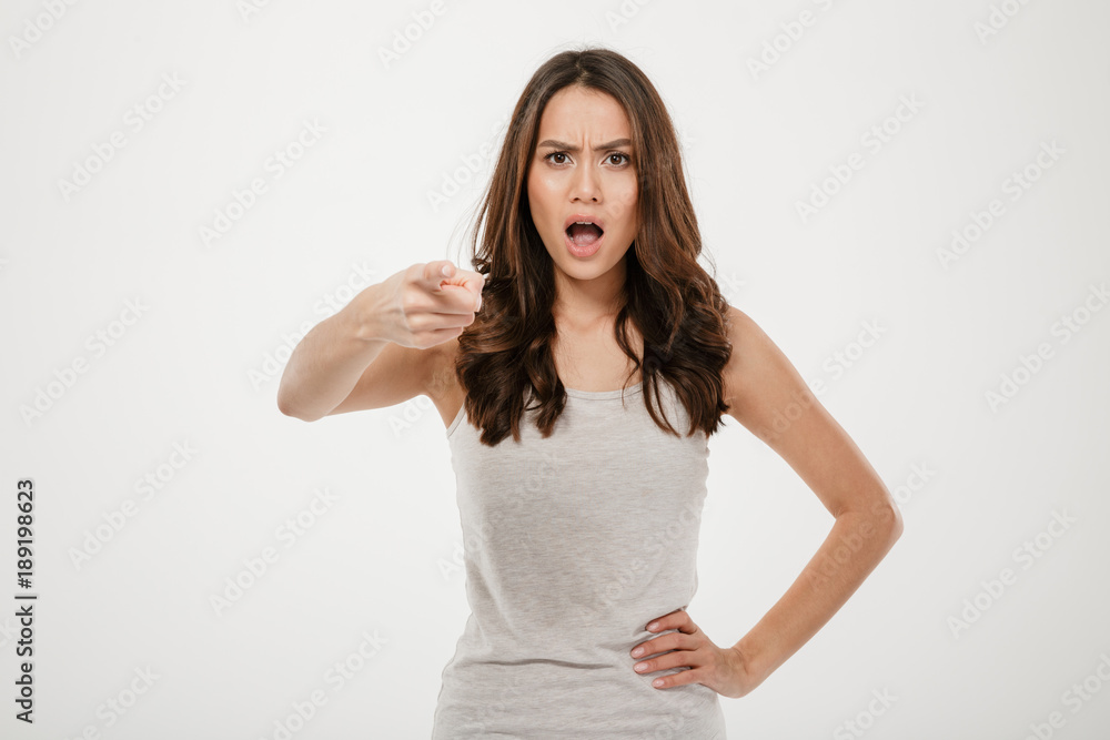 Displeased brunette woman with arm on hip pointing at camera Displeased brunette woman with arm on hip pointing at camera
