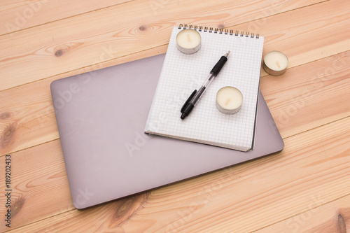 Laptop, notepad, candles and pen on the wooden background