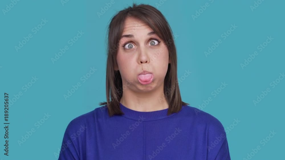 Portrait of hilarious female in casual making faces grimacing on camera having fun being childish over blue background. Concept of emotions Portrait of hilarious female in casual making faces grimacing on camera having fun being childish over blue background. Concept of emotions
