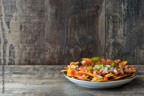 Mexican nachos with beef, guacamole, cheese sauce, peppers, tomato and onion in plate on wooden table