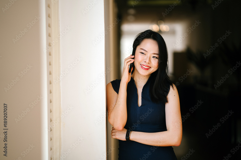 Portrait of a professional businesswoman standing in the middle of a corridor and talking on the phone. She appears to be smiling. Portrait of a professional businesswoman standing in the middle of a corridor and talking on the phone. She appears to be smiling.