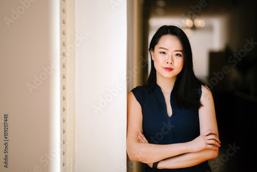 Young attractive business woman leaning against a white wall in a corridor. She looks professional and serious.