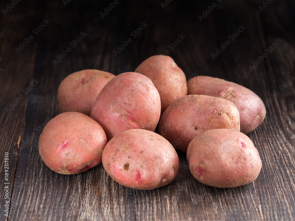 Raw whole organic potatoes on old brown wooden background. Copy space. Low key. Raw whole organic potatoes on old brown wooden background. Copy space. Low key.