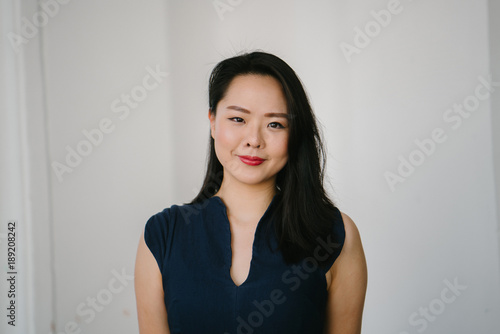 portrait of smart businesswoman standing against a white background. She is looking at the camera and smiling. 