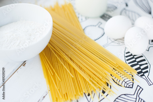 Cooking Homemade Spaghetti with eggs, flour, milk on a white wooden table and white tablecloth with floral pattern