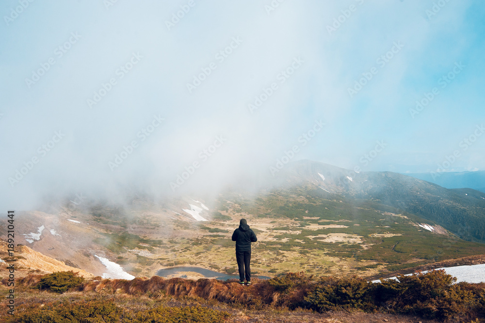 Man standing on a ledge of a mountain, enjoying the beautiful view Man standing on a ledge of a mountain, enjoying the beautiful view