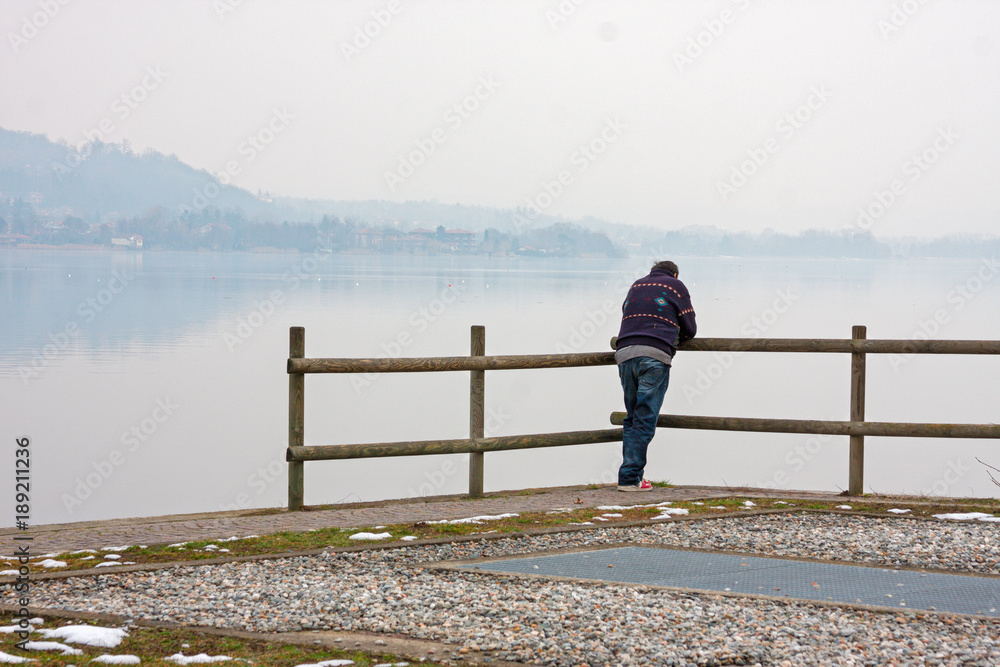 A lonely man looks at the lake leaning against a railing.