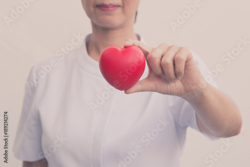 Senior female nurse holding red heart symbol in her hand; isolate on white