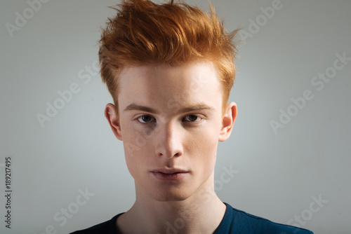Eyes. Good-looking stern dark-eyed red-haired young man wearing a t-shirt and staring and having a modern haircut