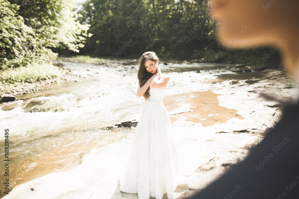 Elegant gentle stylish groom and bride near river with stones. Wedding couple in love Elegant gentle stylish groom and bride near river with stones. Wedding couple in love