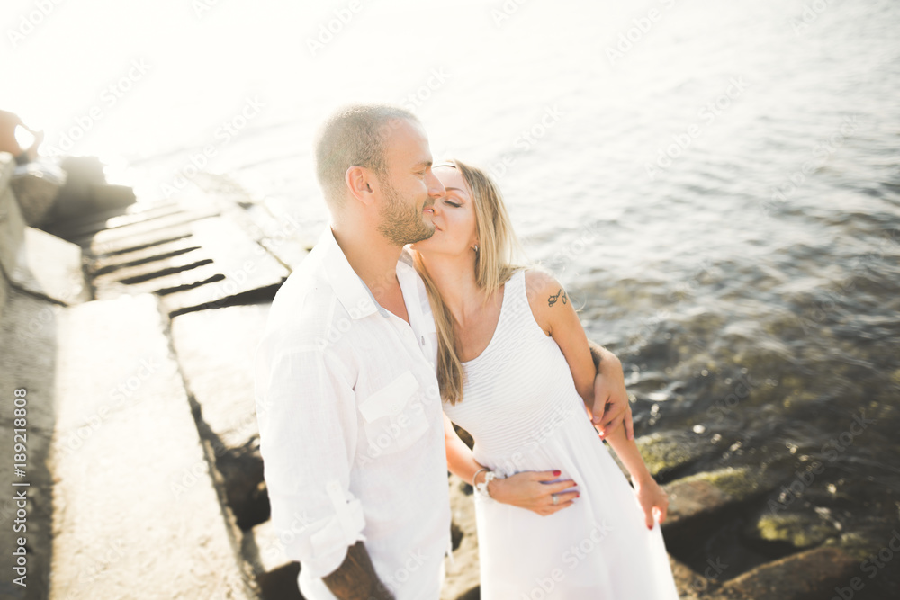 Romantic loving couple posing on stones near sea, blue sky