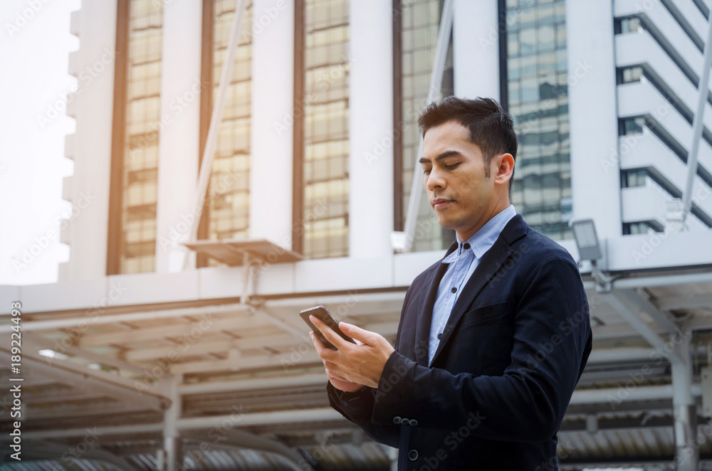 young smart asian business man wearing modern black suit with mobile smart phone in building city background, successful, internet network connection, technology communication, financial concept young smart asian business man wearing modern black suit with mobile smart phone in building city background, successful, internet network connection, technology communication, financial concept