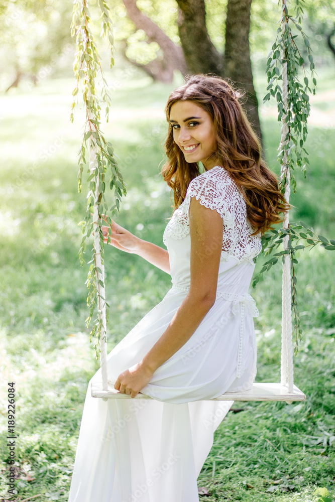 Smiling young girl sitting on the hand made swing in the forest.