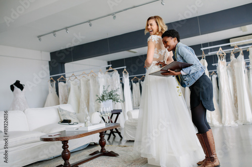 Obraz na plátně Female trying on wedding gown with women assistant in shop