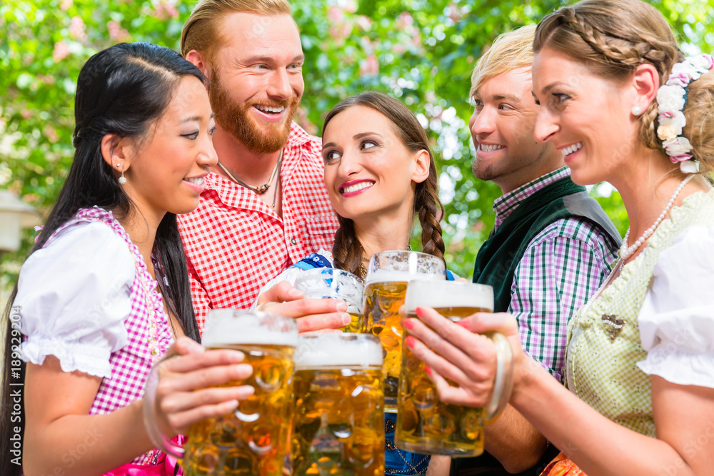 Fünf Freunde in Tracht stoßen mit Bier im Biergarten an Fünf Freunde in Tracht stoßen mit Bier im Biergarten an
