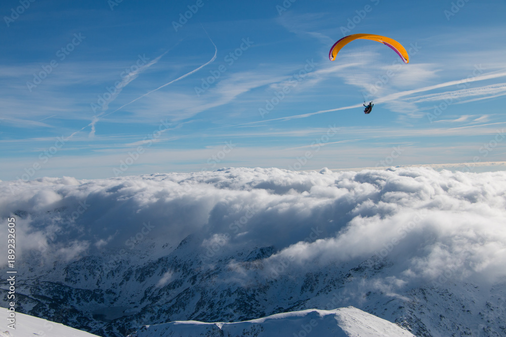 Paragliding above mountain peaks and clouds during winter sunny snowy day Paragliding above mountain peaks and clouds during winter sunny snowy day