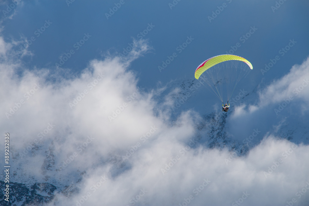Paragliding above mountain peaks and clouds during winter sunny snowy day Paragliding above mountain peaks and clouds during winter sunny snowy day