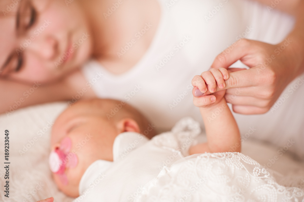 Mother holding baby hand sleeping in bed close up. Motherhood. Maternity. Mother holding baby hand sleeping in bed close up. Motherhood. Maternity.