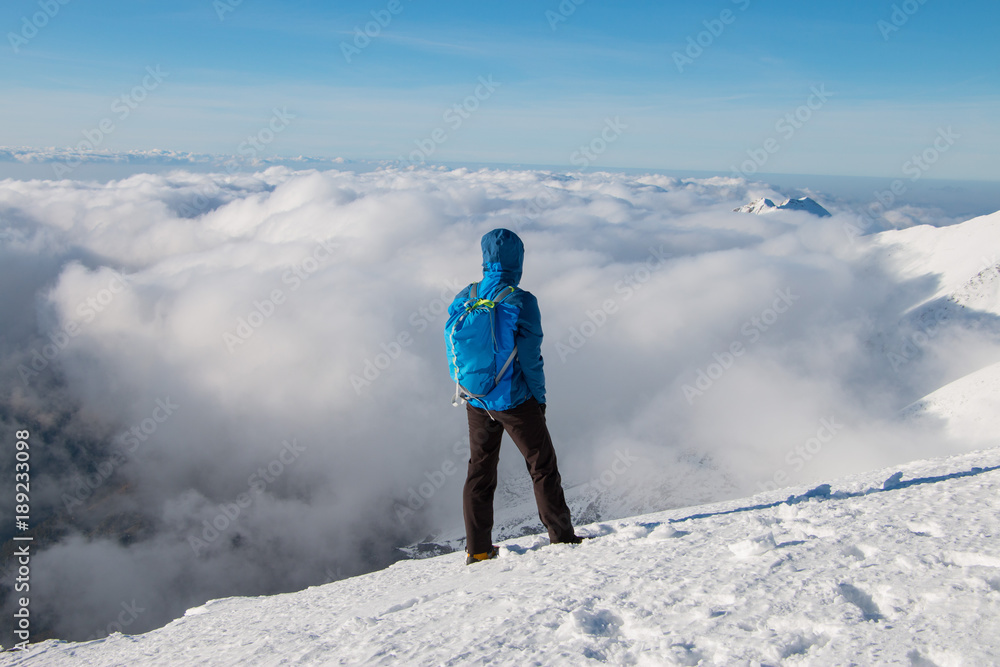 Young happy tourist on top of a snowy mountain enjoying valley view, above the clouds. Conceptual design.