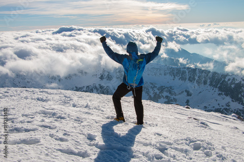Young happy tourist on top of a snowy mountain enjoying valley view, above the clouds. Conceptual design.